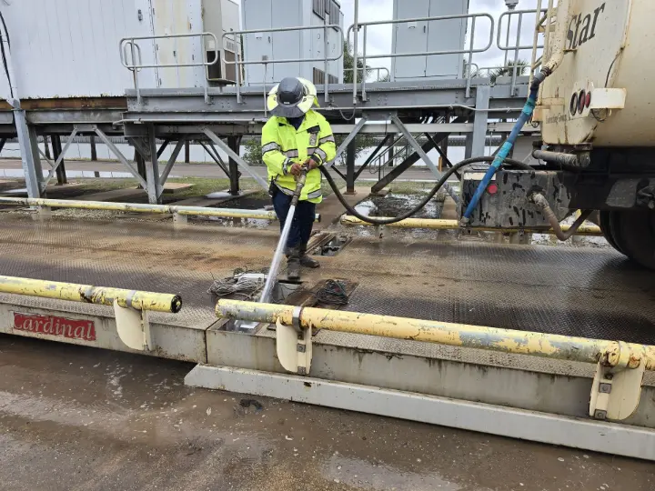 Scale technician using a water truck to clean dirt from a loadcell on a truck scale
